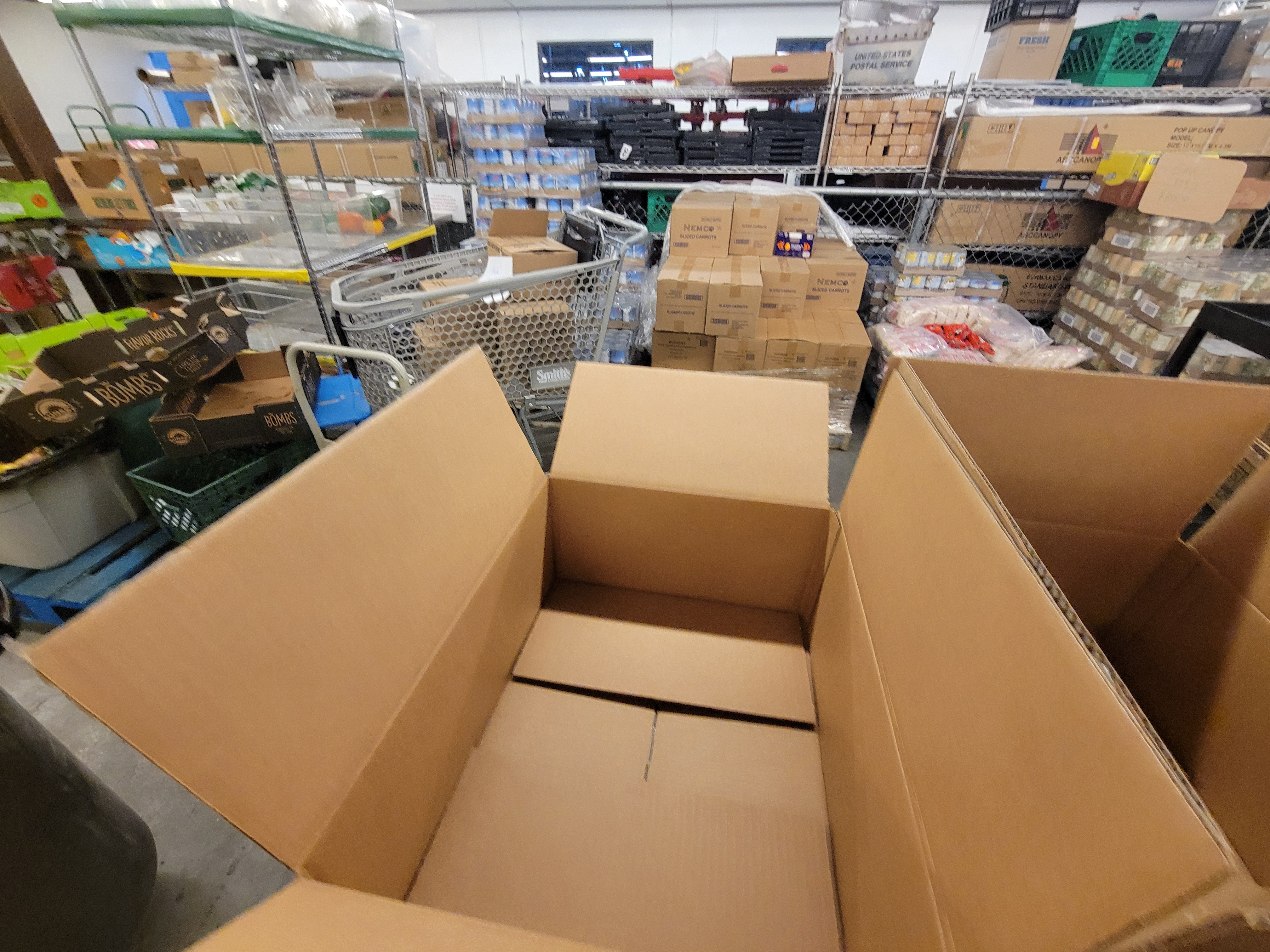 Open box with boxes, pallets of food, and crates in the background.